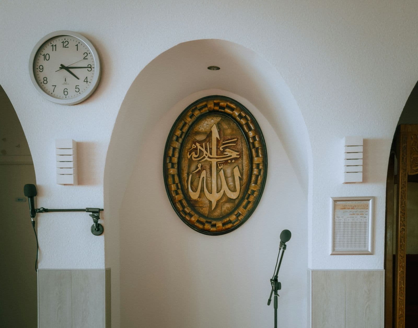 En väggklocka och ett utskrivet månadsschema bredvid mihraben i en liten moské